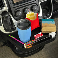 A promaster interior cup holder organizer tray holding a blue tumbler with lid, a red french fries bag, a small notebook, a pink pen, and other small items, shown installed around a gear shift console.