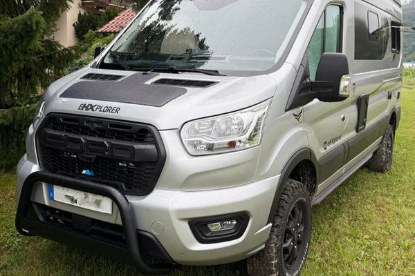 White van with black roof rack on grassy area with trees in the background