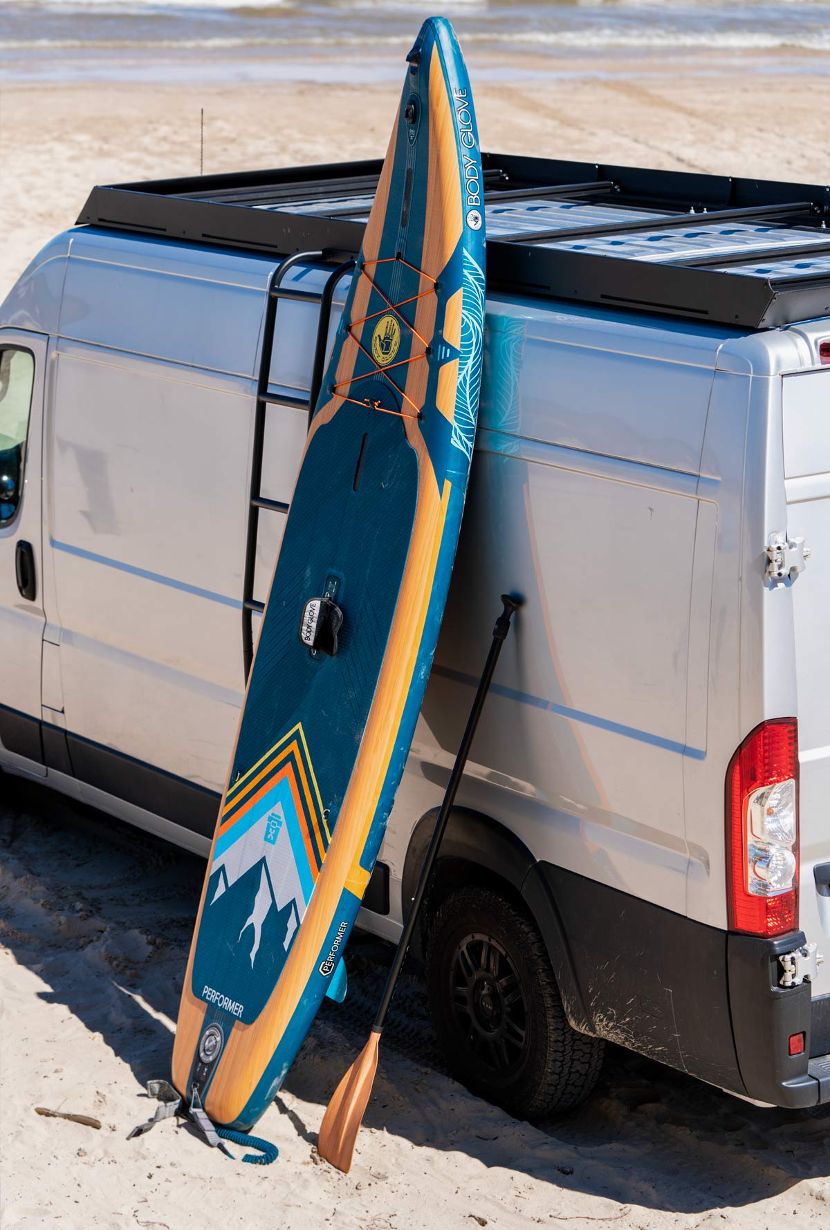 Ram Promaster roof rack by Orion Van Gear at the beach, equipped with a SUP, ready for outdoor adventures and watersport storage.