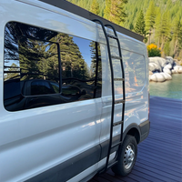 A white van parked on a dark wooden dock with a forest and mountains in the background. A black Orion Van Gear ladder is attached to the side of the van, and the windows reflect the surrounding trees.