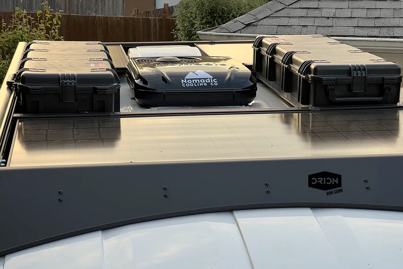 An Orion Van Gear Transit roof rack system carrying two black hard-sided storage cases on a vehicle roof, with flush-mounted solar panels and Nomadic X2 Air Conditioner