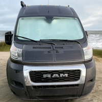 RAM van parked on a sandy beach with ocean in the background - featuring hood solar panel