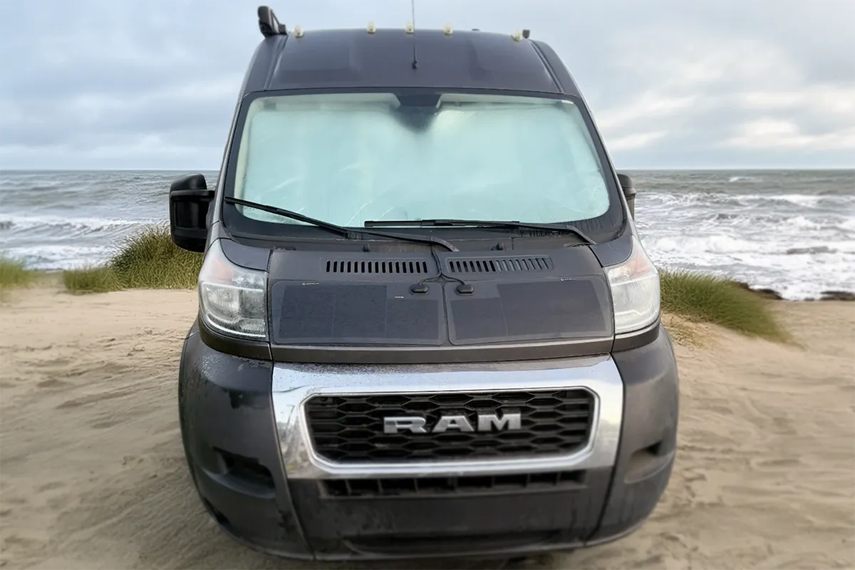 RAM van parked on a sandy beach with ocean in the background - featuring hood solar panel
