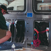 Person working on a van insulation interior with tools and equipment.