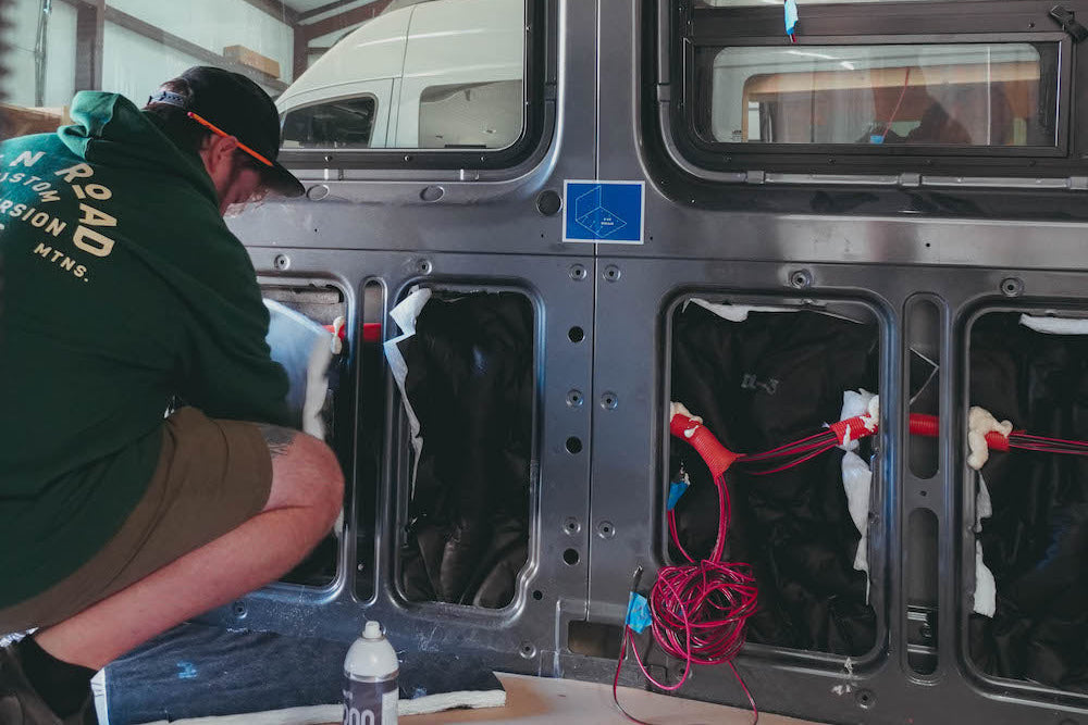 Person working on a van insulation interior with tools and equipment.