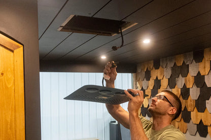 Person installing a nomadic air conditioner faceplate onto wood van ceiling
