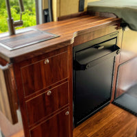 Wooden kitchen counter with a black refrigerator inside a vehicle with folding shower 