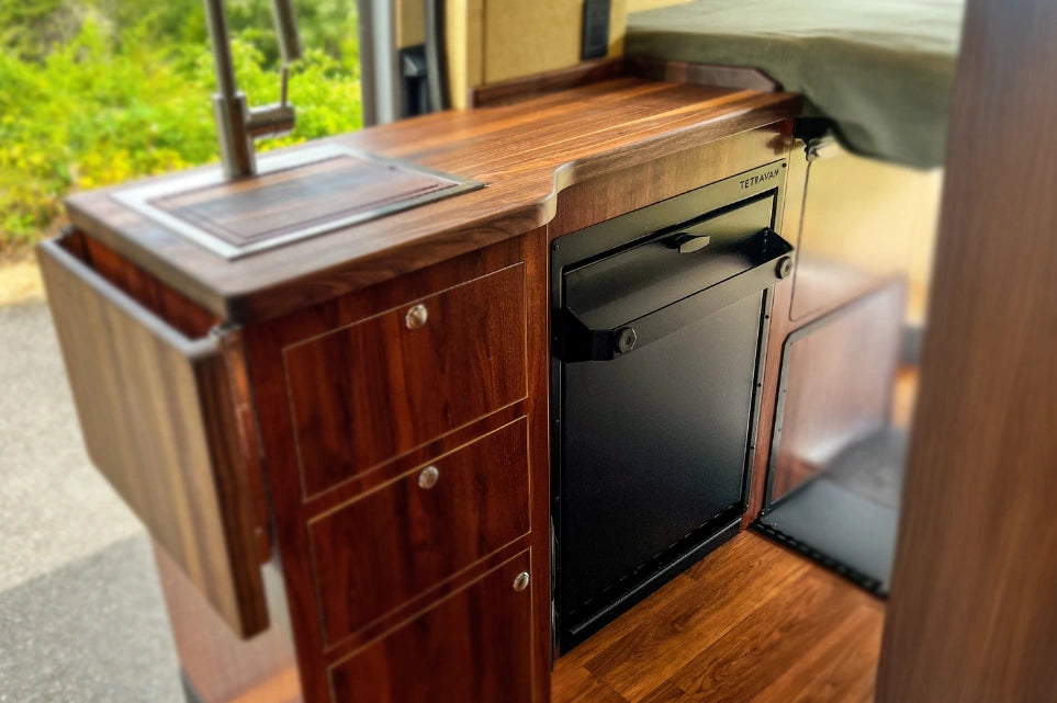 Wooden kitchen counter with a black refrigerator inside a vehicle with folding shower 