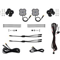 A complete wiring harness kit for vehicle lights, laid out on a clean white background. The kit includes two square LED light modules with attached wiring, two black mounting brackets with screws and washers, several black zip ties, and multiple black wire harnesses with various connector types.