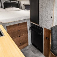 Compact living space with a bed, desk, and storage drawers and folding shower in transit van