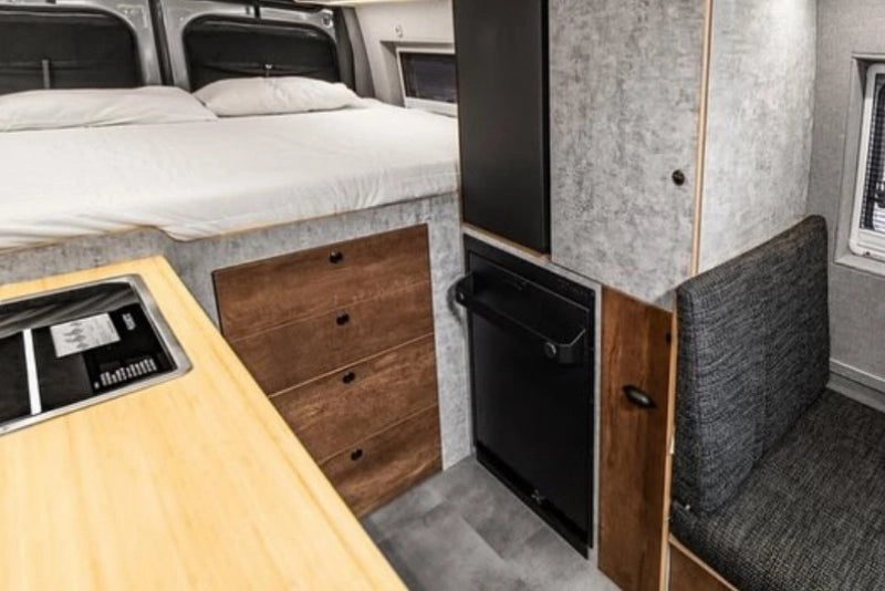 Compact living space with a bed, desk, and storage drawers and folding shower in transit van