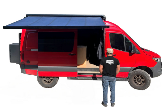 Red van with an extended roof rack and solar panel, person standing nearby wearing a black t-shirt with a logo.