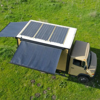 box truck with solar panels on the roof and solar awning on side and rear in a grassy field