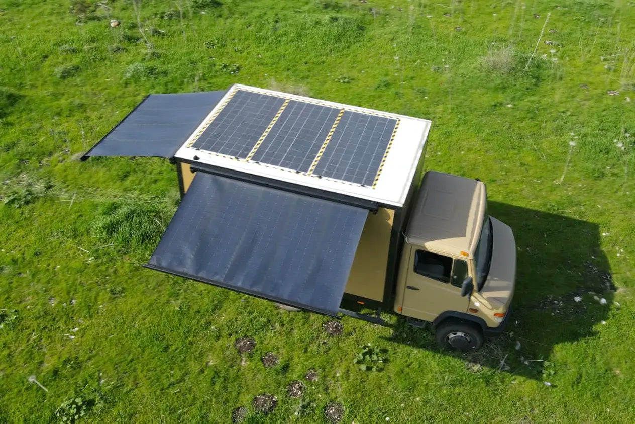 box truck with solar panels on the roof and solar awning on side and rear in a grassy field
