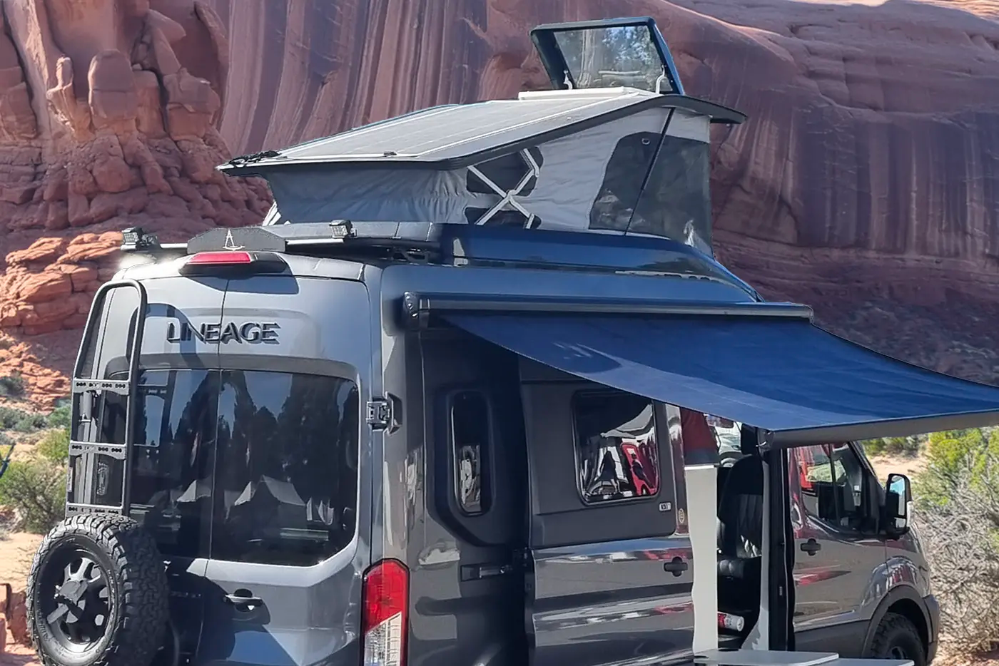 Black off-road vehicle with a roof rack and extended solar awning in a desert landscape.