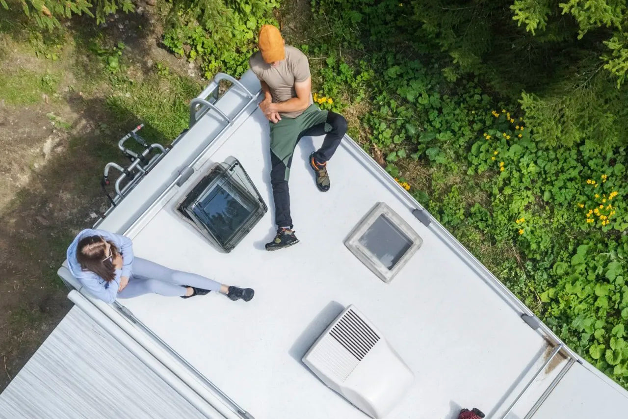 Aerial view of an RV roof with skylights installed, showing a camper setup with people relaxing outside
