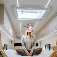 Woman sitting on a van bed looking up at a NomadicArk 700 x 500mm skylight installed in the roof