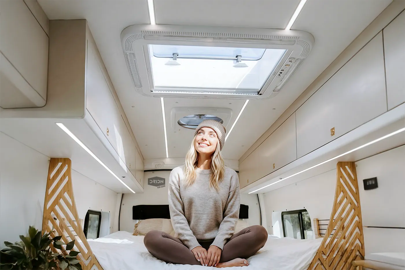 Woman sitting on a van bed looking up at a NomadicArk 700 x 500mm skylight installed in the roof