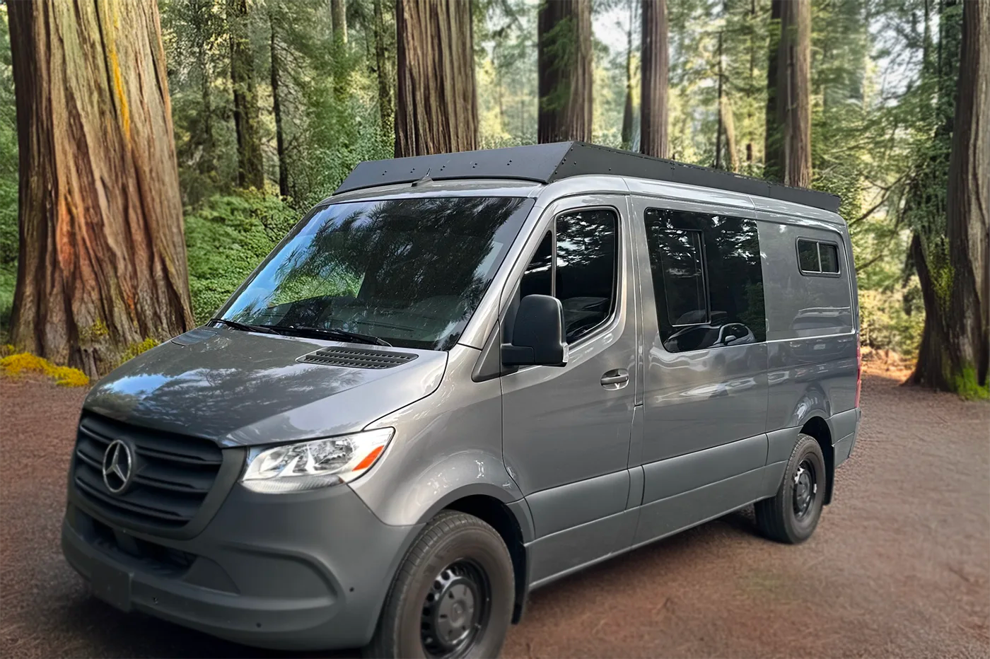 A gray Mercedes-Benz Sprinter Low Standard Roof van parked on a dirt path surrounded by tall redwood trees in a forest with orion van gear roof rack