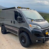 Gray promaster low roof 118 van with off-road modifications on a dirt road with a scenic background