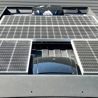 A close-up view of a ram promaster van roof rack covered with multiple solar panels mounted on an orion van gear roof rack, with a MaxxAir fan and air conditioner. 