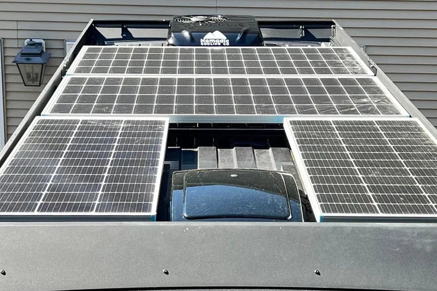 A close-up view of a ram promaster van roof rack covered with multiple solar panels mounted on an orion van gear roof rack, with a MaxxAir fan and air conditioner. 